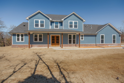 Two-story blue house with white trim, a grey shingled roof, and brown grass in the front yard.