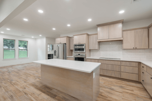 Modern kitchen with light wood cabinets, stainless steel appliances, and a large island.