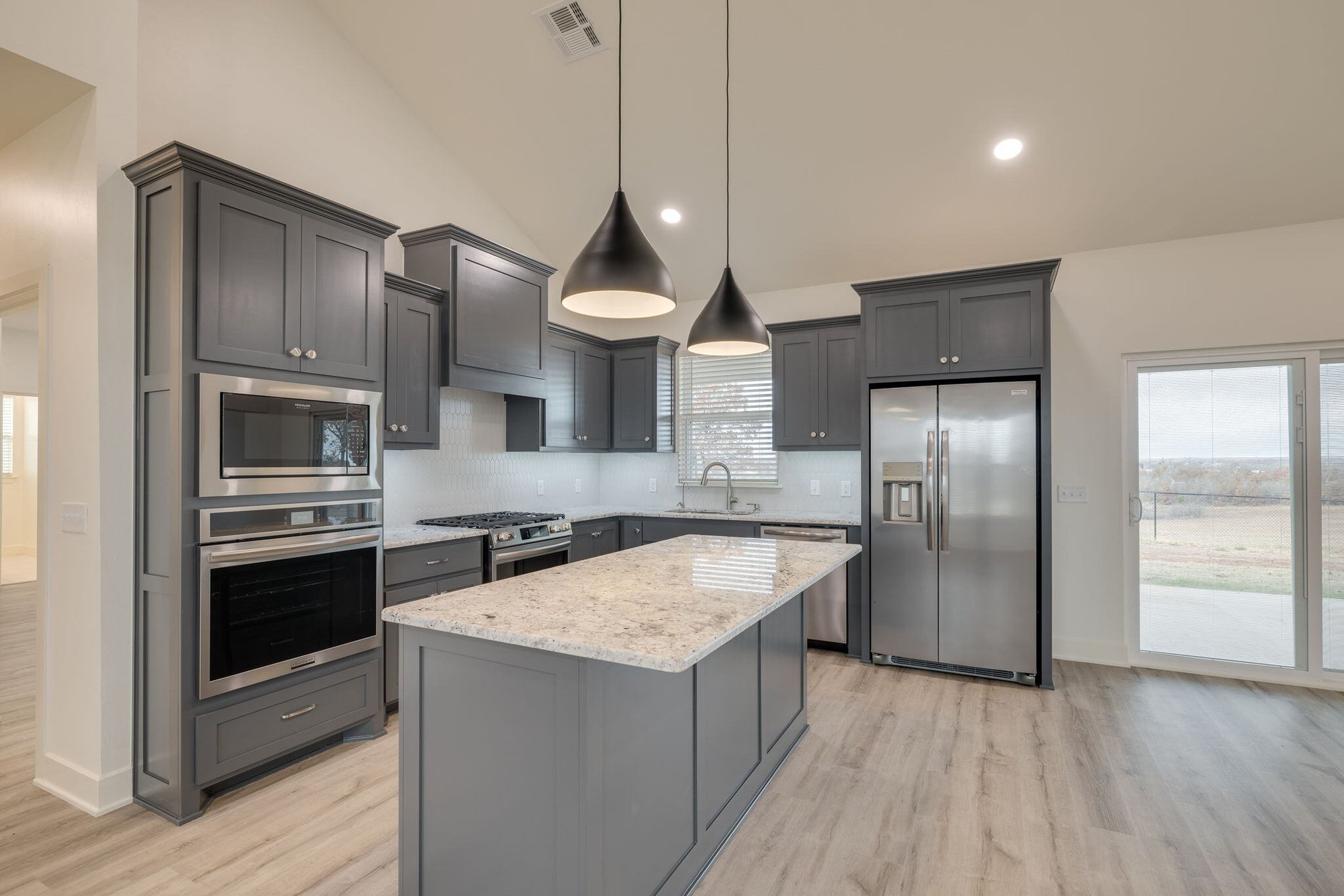 Stainless steel appliances, pendant lighting, and light wood flooring in an open-concept layout.