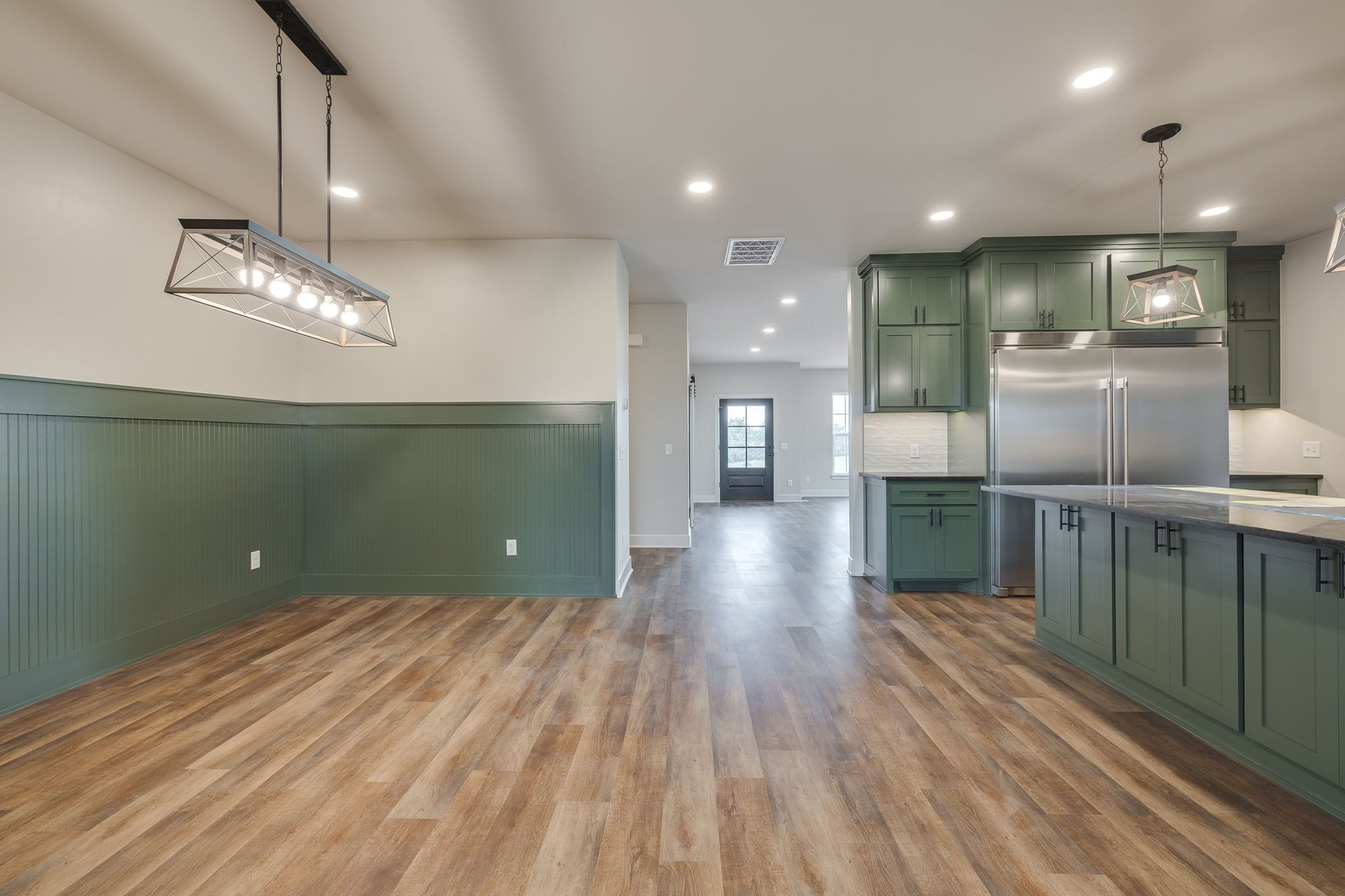 Open-concept kitchen and dining area in Guthrie, Oklahoma, featuring green cabinetry, wood-look flooring, modern pendant lighting, and stainless steel appliances.
