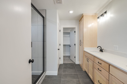 Modern bathroom with glass shower, light wood vanity, and white walls.