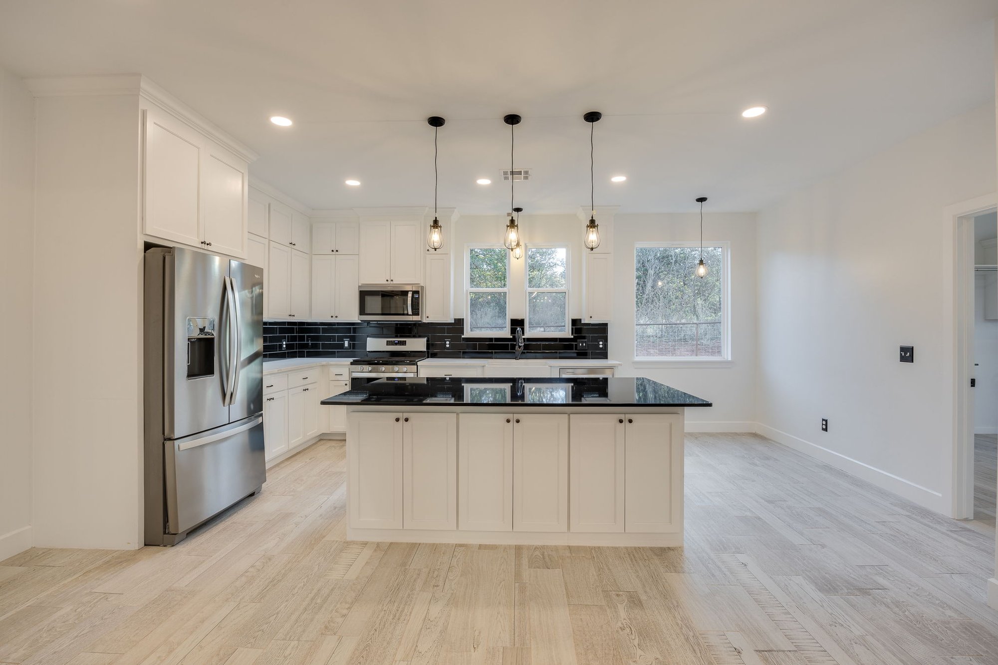 Modern white kitchen with black tile backsplash, stainless steel appliances, and center island in a custom home built in Crescent, Oklahoma.