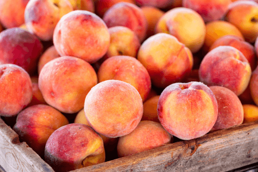 A wooden crate filled with ripe peaches varying in color from yellow to reddish-orange.