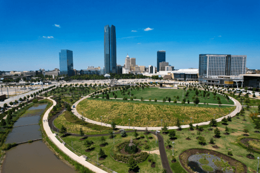 Aerial view of a park with circular grassy area and skyline in the background featuring high-rise buildings.