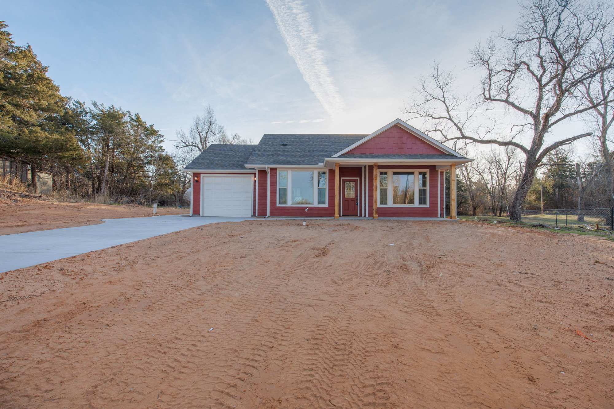 Single-story red custom home with white trim, front porch, and attached garage in Crescent, Oklahoma.