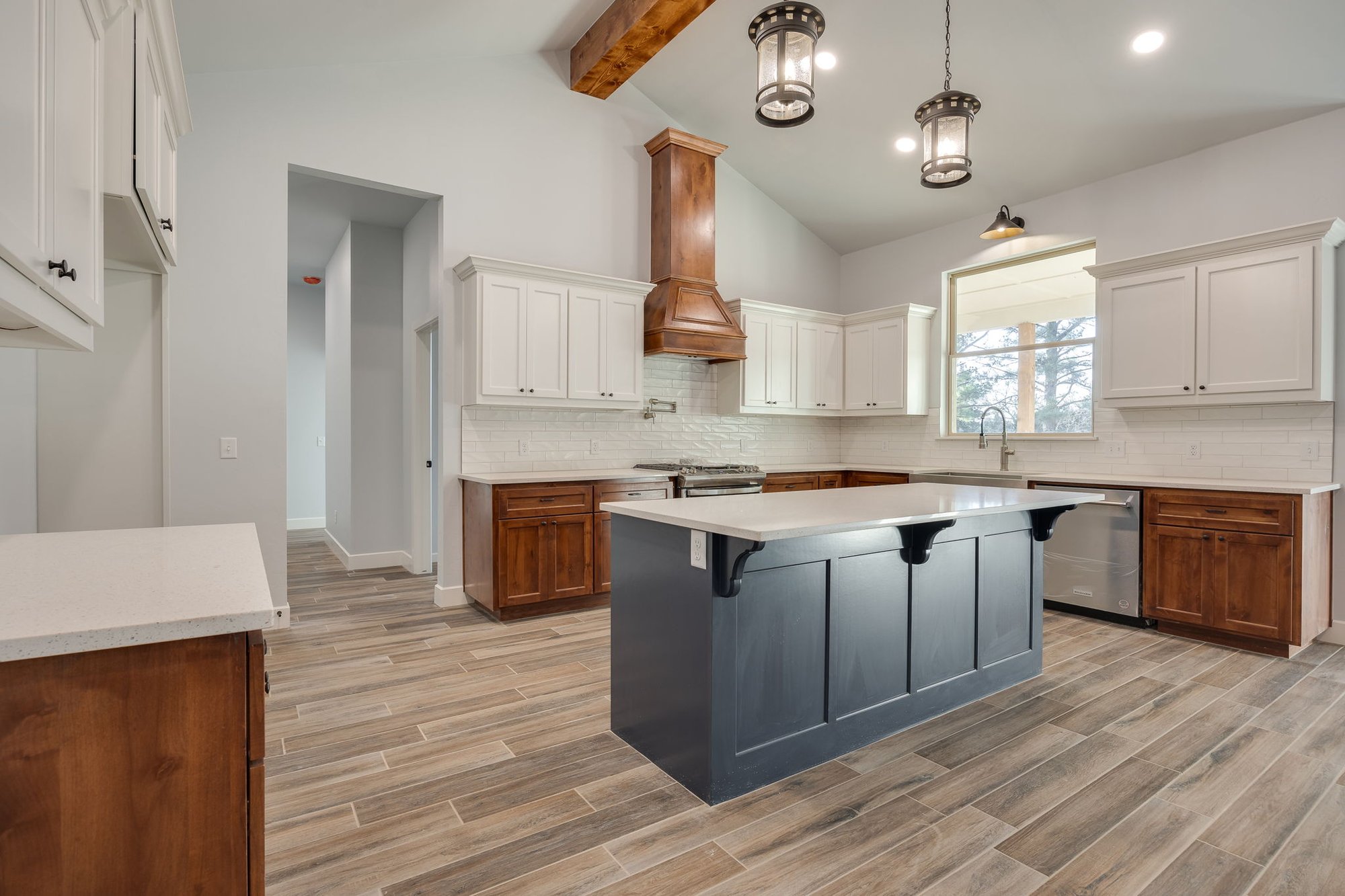 Modern farmhouse-style kitchen with white cabinets, wood range hood, and wood-look tile flooring.