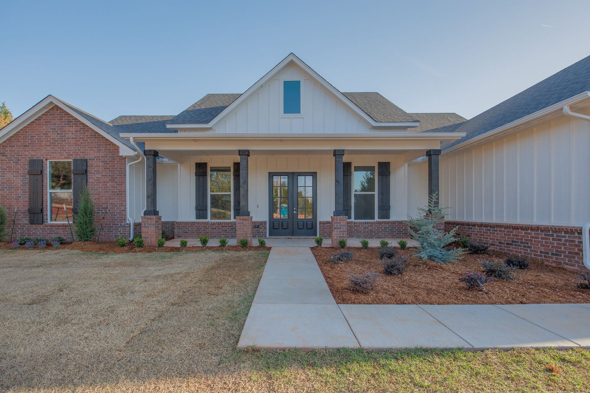Single-story home featuring black shutters, covered porch with dark wood columns, and fresh landscaping.