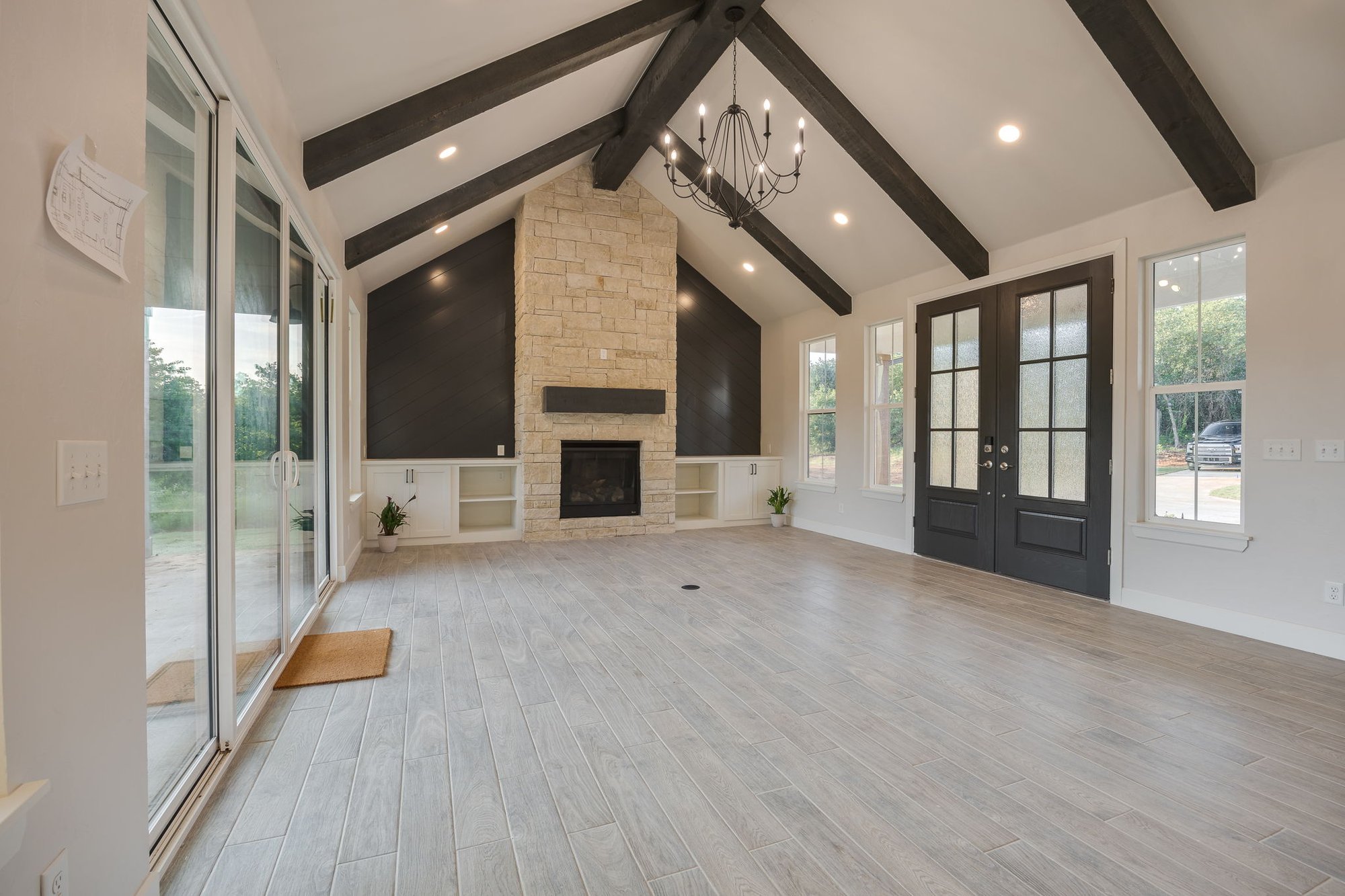 Modern farmhouse space with dark wood beams, chandelier, and sliding glass doors.