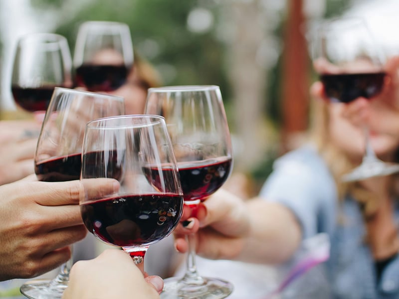 Friends toasting glasses of red wine at an outdoor gathering in Slaughterville, Oklahoma, celebrating under sunny skies.