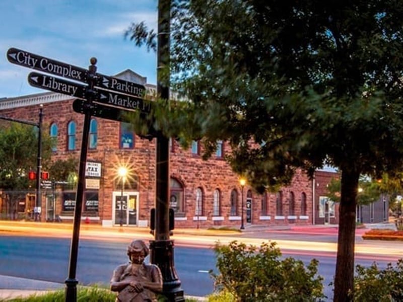 Street view of historic downtown Edmond, Oklahoma, with brick buildings, directional signs, and evening lights.