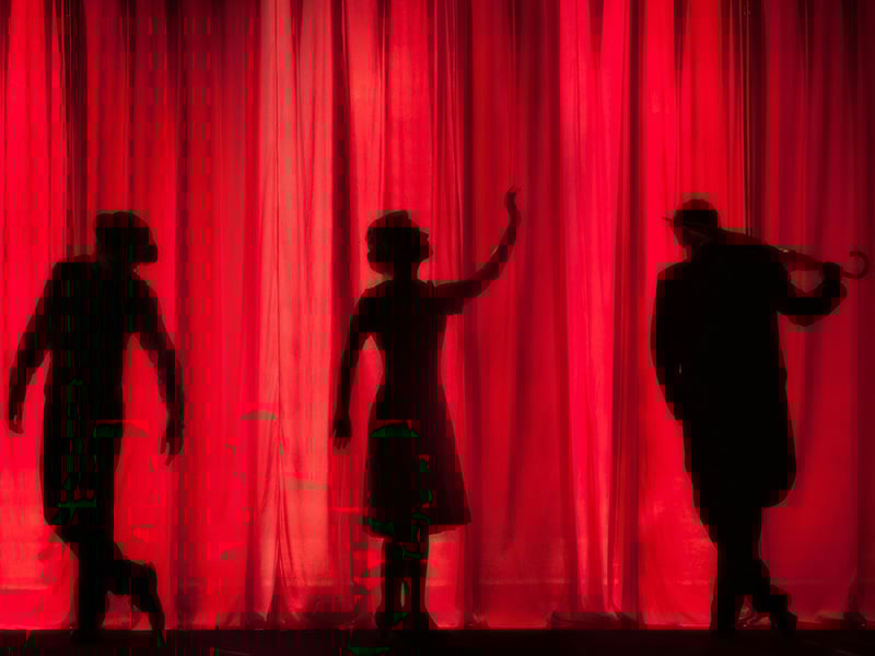 Silhouettes of three performers on stage against a red curtain at the Pollard Theatre in Guthrie, Oklahoma.