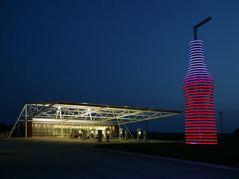 Giant illuminated soda bottle sculpture glowing in red and purple against a dark sky in Arcadia, Oklahoma.